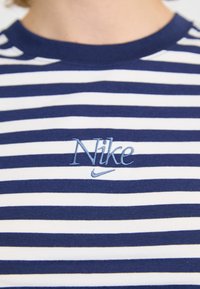 Tamsiai mėlynai ir baltai dryžuota medvilninė marškinėlių suapvalinta kaklo iškirpte, su mėlynai siuvinėtu Nike logotipu ant krūtinės.