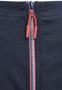 Tissu bleu marine avec une fermeture éclair centrale mettant en valeur des accents rouges et des dents multicolores. Le tirette de la fermeture éclair est rouge avec une finition texturée.