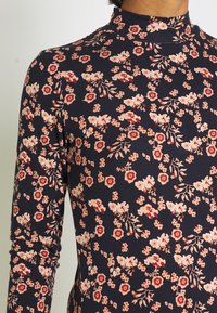 Blommig långärmad topp i marinblå, med en hög krage, prydd med persikofärgade och röda blommor samt gröna detaljer på ett mjukt, texturerat tyg.