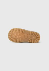 Semelle crantée d'une botte marron clair, présentant des rainures profondes et des motifs croisés pour une adhérence sur un fond blanc uni.