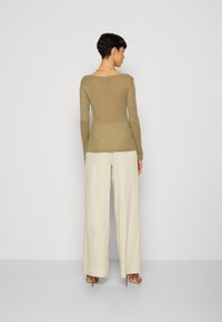 Oliven grønn langermet topp med rund hals, kombinert med kremfargede vide bukser og beige hælsandaler. Minimalistisk design og myk tekstur.