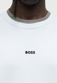 Φωτεινό γαλάζιο t-shirt με στρογγυλή λαιμόκοψη και γκρι γιακά· διαθέτει μαύρο λογότυπο "BOSS" στο μπροστινό μέρος, με λεία υφή.