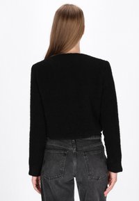 Zwarte cropped sweater van een textuurstof met lange mouwen en een ronde halslijn, gecombineerd met hoog-getailleerde grijze jeans met achterzakken.
