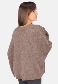 Brauner, grob gestrickter Pullover aus dicker Wolle, mit lockerer Passform und weiten Ärmeln. Die Textur wirkt warm und gemütlich, ideal zum Schichten.
