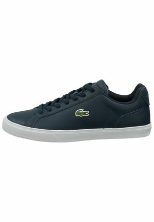 Marineblauwe lage sneaker met witte zool, veters aan de voorkant en groen krokodillenlogo aan de zijkant.