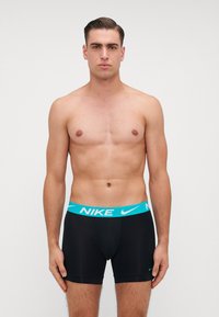 Pánske čierne boxerky s modrým pásom s logom Nike, priliehavý strih, hladká textúra a krátke nohy. Žiadne vnútorné detaily ani vzory.