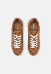 Baskets brunes avec un dessus à motifs, lacets blancs et une semelle blanche légèrement surélevée. Comprend un matériau texturé et un logo sur la semelle intérieure.