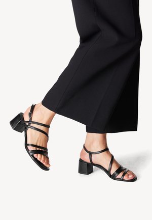 Zwarte sandalen met banden en een blokhak, met fijne banden over de voet en enkel. Het materiaal lijkt glad met een matte afwerking.