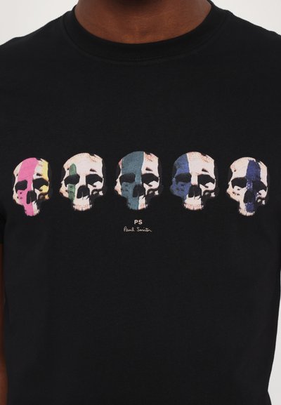 Svart bomull t-shirt med fem stiliserade dödskallar med färgglada accenter i rosa, grönt, blått och ljusrosa, med "PS Paul Smith" tryckt nedanför.