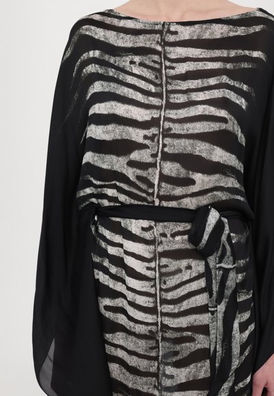 Bluză neagră din material transparent, cu un model de dungi zebra în nuanțe de gri. Prezintă un decolteu rotund și o curea legată în talie. Logo-ul brandului este vizibil subtil.