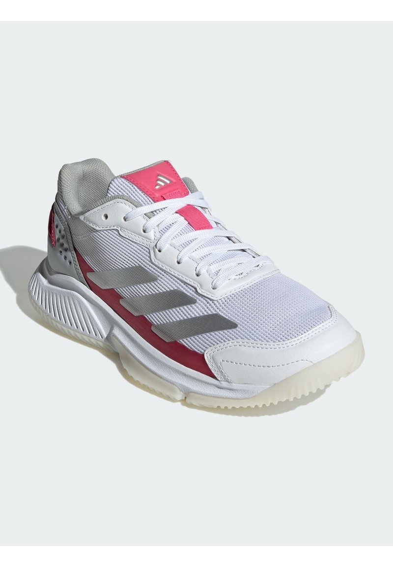 Zapatilla deportiva blanca con parte superior de malla, acentos rosas y talón gris. Presenta tres rayas grises, suela texturizada y sistema de cordones tradicional.