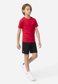 T-shirt rouge à manches courtes, short noir et baskets blanches avec des accents bleus ; tous avec des détails de logo. Tissu lisse, coupe décontractée.