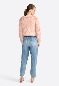 Maglione rosa peloso con design cropped, abbinato a jeans high-waisted di un blu chiaro con vita elasticizzata e tasche posteriori.