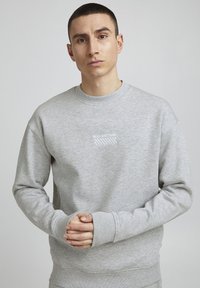 Sweatshirt gris en tissu doux, avec un col rond, des manches longues et un texte brodé blanc "SLD-EST.1999" sur le devant.