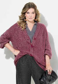 Bordeauxfärgad stickad cardigan med tre knappar, oversized passform och ribbat mönster. Kombinerad med mörka texturerade byxor och en svart kuvertväska.