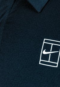 Svart Nike polo skjorte med klassisk krage og en hvit logo design på venstre side. Stoffet har en subtil tekstur.