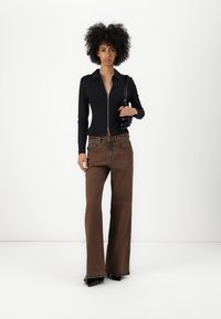 Black zip-up long-sleeve top with a collar, paired with high-waisted, flared brown jeans. Model holds a black handbag, featuring sleek lines.