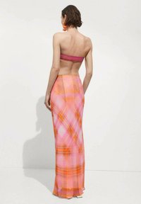 Jupe maxi en tissu rose transparent avec des motifs orange et en Vichy, présentant une silhouette ajustée et un ourlet simple. Dos uni et texture lisse.