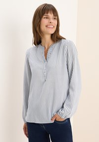 Blouse rayée en bleu clair et blanc, avec un col henley, des manches longues avec des poignets élastiques et des détails de boutons au col.