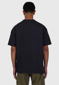 Schwarzes Baumwoll-T-Shirt mit lockerer Passform, kurzen Ärmeln und geradem Saum. Sichtbare Nähte an den Kanten und eine glatte Textur.