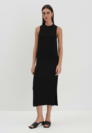 Abito nero senza maniche con un motivo a maglia testurizzato, caratterizzato da una silhouette dritta e uno spacco laterale, abbinato a sabot neri.
