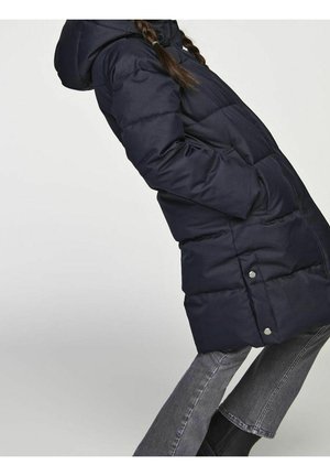 Manteau matelassé bleu marine avec capuche, présentant des panneaux matelassés et des accents à boutons pression. Texture lisse, longueur jusqu'aux genoux, et poches latérales.