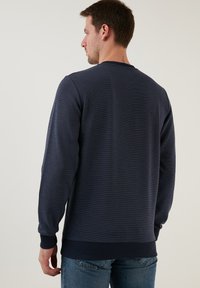 Jūras spēku stila džemperis ar teksturētu apdari, ribotām piedurknēm un apakšmalu, apaļu kakla izgriezumu un brīvu piegriezumu. Standarta redzējums no aizmugures.