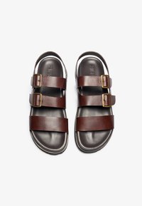 Brown leather sandals with two adjustable buckle straps, a smooth footbed, and a black rubber sole, designed for comfort and stability.