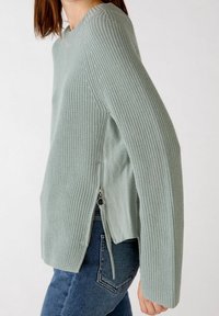 Light green knitted sweater featuring a round neckline, dropped shoulders, and side zippers. The fabric has a textured rib pattern.