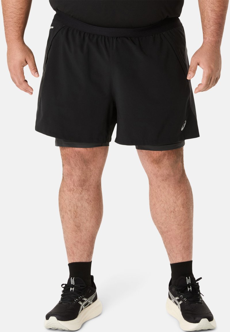 Zwarte sportshorts met een elastische tailleband, voorzien van zijzakken en een lichtgewicht stof. Draag met zwarte sneakers en sokken.