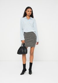 Vaaleansiniset raidalliset pitkät hihaset polo-paidat, harmaa tekstuuri-helma, musta laukku kerätyllä ylhäällä, mustat sukat ja kärkitossut.