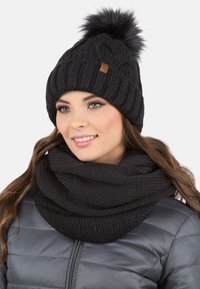 Zwarte gebreide beanie met een pompon en een gestructureerd patroon, gecombineerd met een bijpassende zwarte gebreide infinity-sjaal.