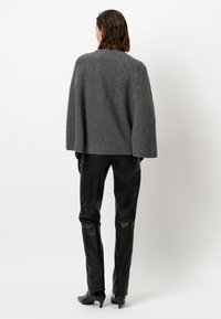 Grijze, oversized gebreide trui met ribbeltextuur, voorzien van een hoge kraag en verlaagde schouders, gecombineerd met zwarte, strakke leren broeken.
