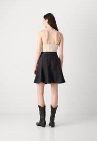 Haut ajusté beige avec des fines bretelles, associé à une jupe noire évasée. Le mannequin porte des bottes de cowboy noires ; tissu lisse avec une texture subtile.
