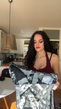 Svart och gråmönstrad jacka med slät textur, med fodrad insida, huva och elastiska manschetter, visad mot en köksbakgrund.