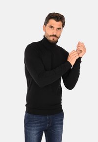 Maglione a collo alto nero realizzato in un morbido e elastico tessuto a maglia, design aderente con polsini e orlo a coste, abbinato a jeans in denim blu.