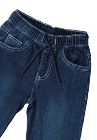 Joggers de mezclilla en azul oscuro con una banda elástica en la cintura, cordón y dos bolsillos frontales; cuenta con costuras visibles y una textura suave.