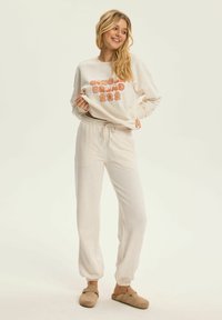Kremowa bluza z napisem "GINGERBREAD" i grafiką postaci pierniczka, w komplecie z pasującymi kremowymi dresami z elastycznym pasem.