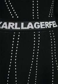 Tissu noir avec des lignes blanches en pointillés verticales et une ceinture côtelée présentant du texte blanc partiellement visible.