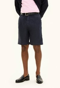 Shorts in lino blu navy con una vestibilità comoda, dotati di tasche laterali e una texture liscia, abbinati a mocassini in pelle nera.