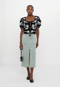 Μαύρη βελούδινη κοντή μπλούζα με κεντητά λουλούδια, σε συνδυασμό με μια ανοιχτό γαλάζια τζιν φούστα μίντι με ασημένιες λεπτομέρειες και μπροστινό σκίσιμο.