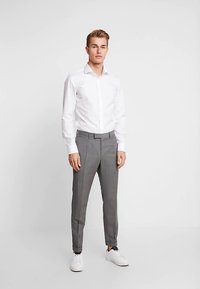 Biała koszula zapinana na guziki w połączeniu z szarymi, dopasowanymi spodniami w delikatny wzór. Dopełnieniem są białe trampki, które dodają casualowego charakteru.