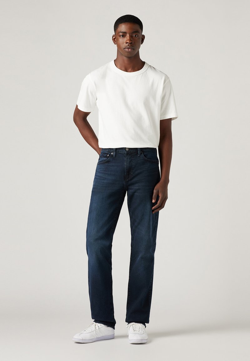 Camiseta de algodón blanca, vaqueros de denim azul oscuro y zapatillas blancas. Corte recto, diseño sencillo y líneas limpias.