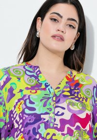 Multikleurige blouse met wervelingen en abstracte patronen in levendig groen, paars, rood en blauw. Korte mouwen en een kleine knoopsluiting.