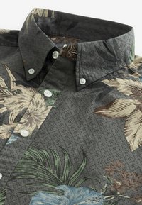 Camisa con estampado floral en tejido gris oscuro, con cuello flexible, botones blancos y superficie texturizada con motivos de plantas.