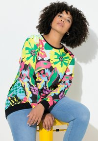 Sweatshirt à manches longues coloré avec de grands motifs floraux en jaune, rose, vert et bleu sur un fond noir. Poignets noirs côtelés.