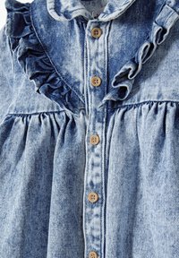 Denimmekko, jossa on röyhelökaulus, nappisulku ja laskostettu hame. Väri on vaaleansininen, ja siinä on vaihtelevia farkkotekstuureja.