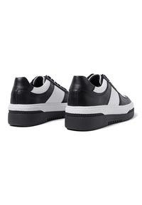 Sneaker bianco e nero con una tomaia in pelle liscia, dettagli testurizzati, una suola spessa e un design classico con lacci.