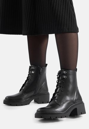 Czarne skórzane botki za kostkę z wiązaniem z przodu, bocznym zamkiem błyskawicznym, masywnym obcasem i teksturowaną gumową podeszwą. Posiadają metalowe przelotki i ozdobne przeszycia.