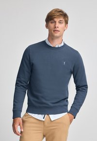 Marinblå sweatshirt i bomullsmix, med rund hals och ribbade mudd. En liten logotyp är broderad på bröstet.